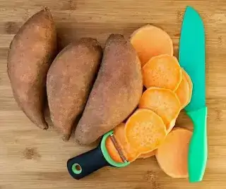Fresh orange sweet potatoes sliced on a wooden board with a knife showing the bright orange flesh inside